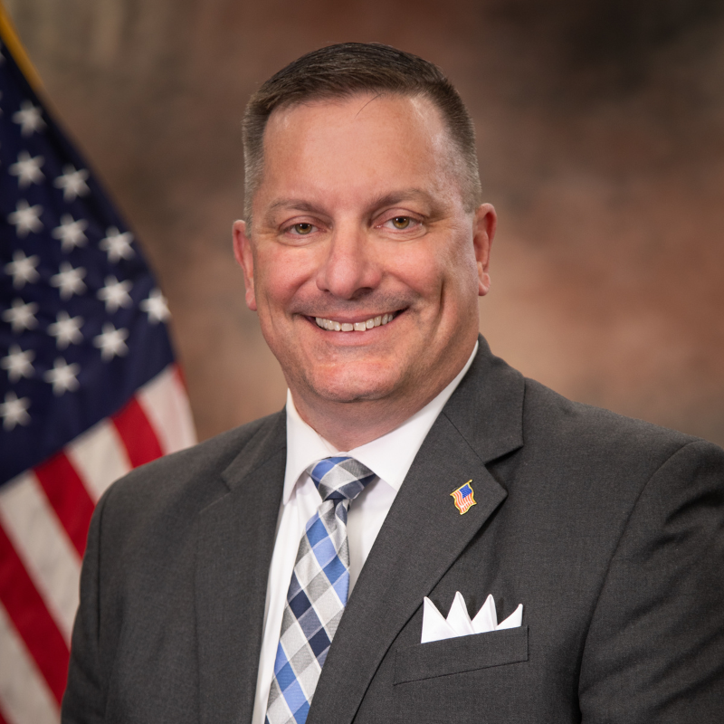 headshot photo of Patrick Mirandy with American flag in background