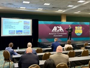 Assistant Sheriff Nate Wilson speaking at a conference on stage with ACA background