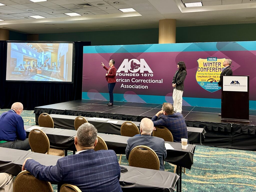 three people giving a presentation on stage with American Correctional Association background