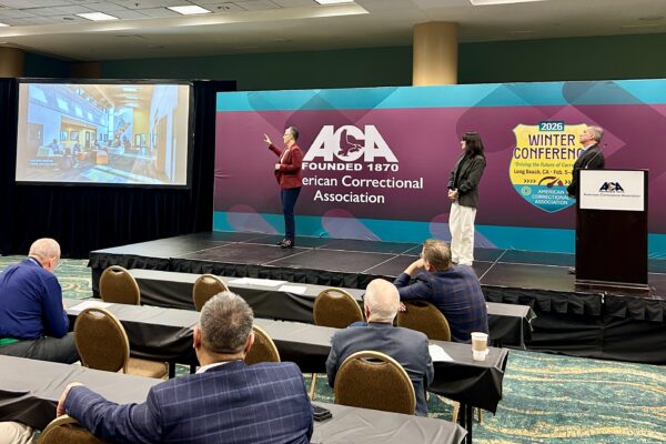 three people giving a presentation on stage with American Correctional Association background