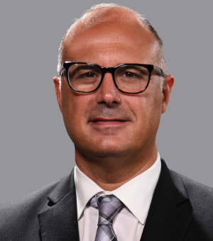 headshot photo of Dan Martuscello wearing glasses and suit and tie with gray background