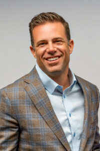 headshot of Darrick Hutchens wearing plaid suit jacket and blue shirt
