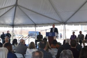 man in suit addresses crowd at ribbon cutting event