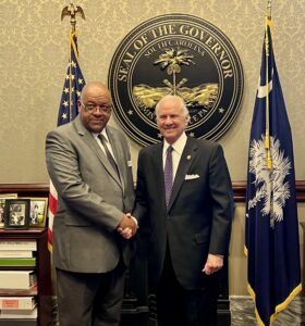 Dennis R. Patterson Sr. shaking hands with Gov. Henry McMaster is front of South Carolina state seal