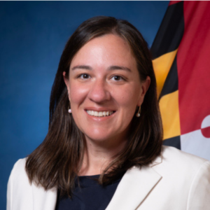 headshot of Betsy Fox Tolentino with blue background and Maryland state flag