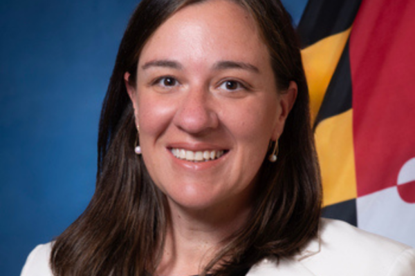 headshot of Betsy Fox Tolentino with blue background and Maryland state flag