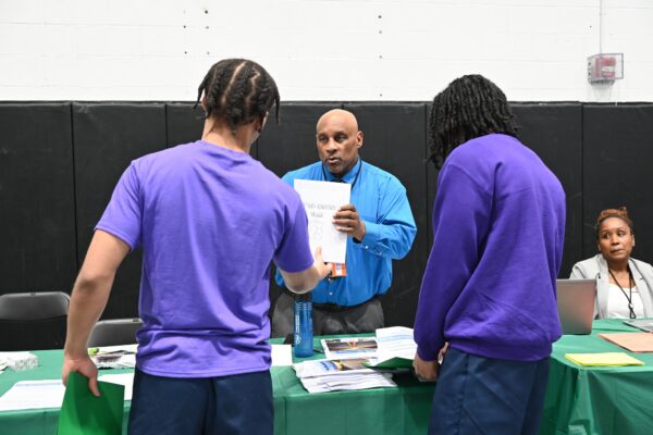 two youth in blue shirts speaking to a man at a reentry fair