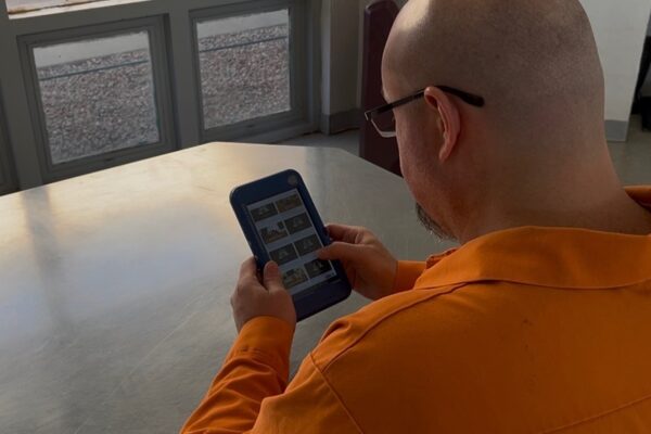 inmate in orange jumpsuit seated at a table using a tablet