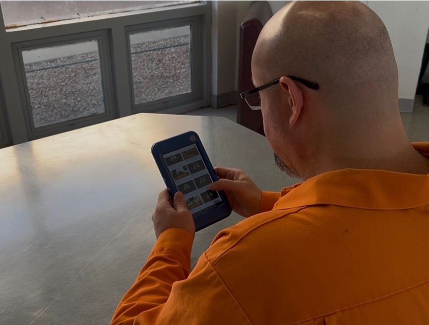 inmate in orange jumpsuit seated at a table using a tablet