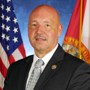 headshot photo of Ricky Dixon with USA and Florida flags in background