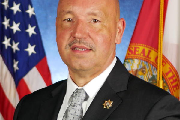 headshot photo of Ricky Dixon with USA and Florida flags in background