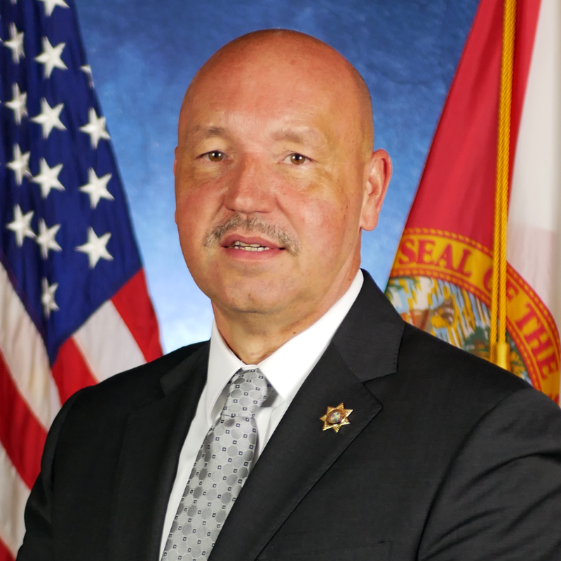 headshot photo of Ricky Dixon with USA and Florida flags in background